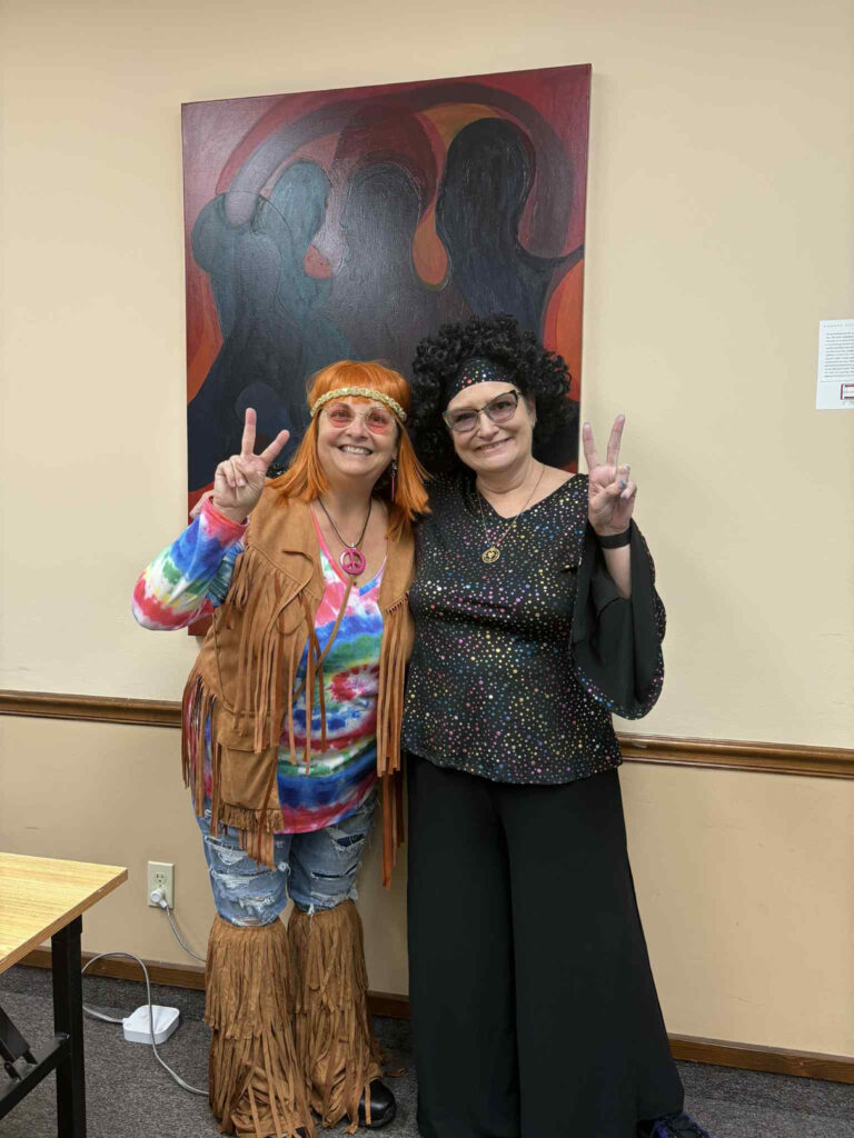Last month, two women in 1970s-style costumes smiled and made peace signs at a Lunch & Learn. One wore a tie-dye shirt, fringe vest, and headband; the other sported a sparkly black outfit and round glasses in front of abstract artwork. -WorkIT Coworking Center