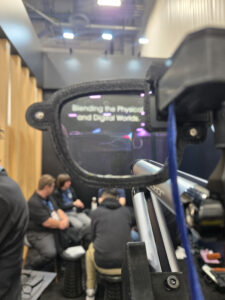 A transparent augmented reality lens displays the text Kristen's Corner: Blending the Physical and Digital Worlds while several people sit and talk in a modern indoor setting in the background. -WorkIT Coworking Center