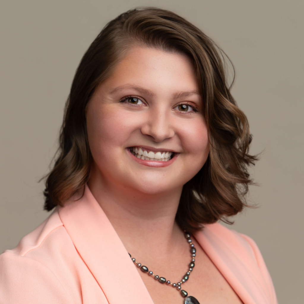 Smiling woman with short brown hair, Keri Garrison, Member of the Month, wears a light pink blazer and a beaded necklace, posed against a plain beige background. -WorkIT Coworking Center